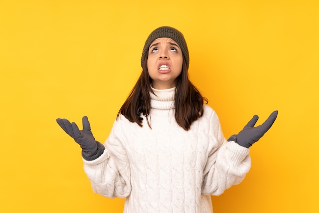 Mujer joven con sombrero de invierno sobre fondo amarillo aislado frustrado por una mala situación