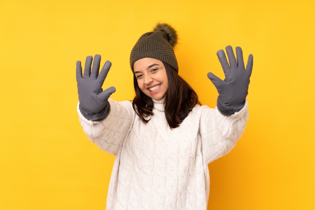 Mujer joven con sombrero de invierno sobre pared amarilla aislada contando diez con los dedos