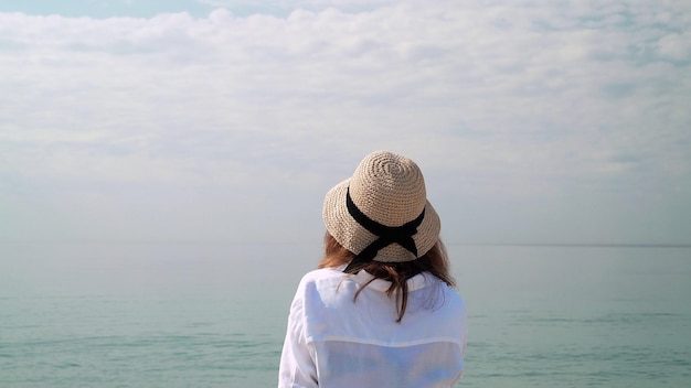 mujer joven, en, sombrero de mimbre, cerca, océano, espalda, tiro, en, plano de fondo, de, cielo, y, mar