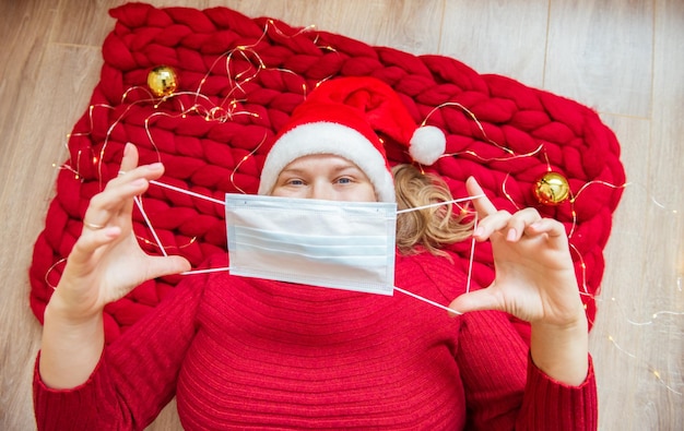 Mujer joven con sombrero de Navidad se quita o se pone máscara protectora