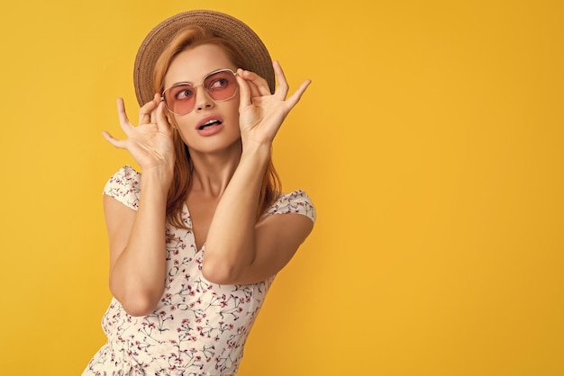 Mujer joven con sombrero de paja y gafas de sol sobre fondo amarillo