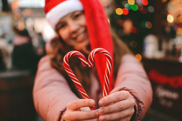 Una mujer joven con un sombrero de Papá Noel muestra un símbolo de corazón hecho con bastones de caramelo