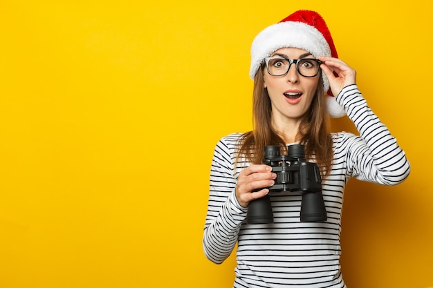 Mujer joven con un sombrero de Papá Noel tiene binoculares