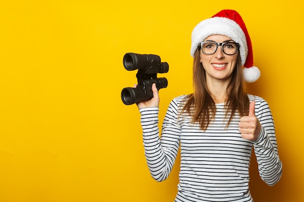 Mujer joven con un sombrero de Papá Noel tiene binoculares