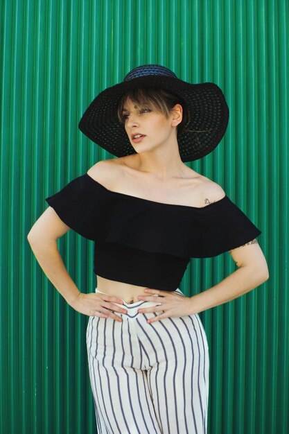 Foto mujer joven con sombrero de pie contra la pared