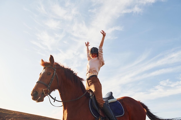 Mujer joven con sombrero protector con su caballo en el campo agrícola durante el día soleado