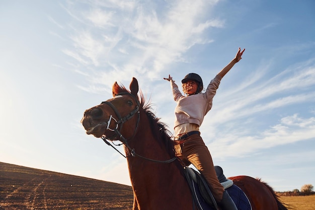 Mujer joven con sombrero protector con su caballo en el campo agrícola durante el día soleado