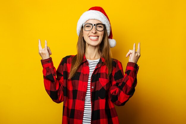 Mujer joven con sombrero de santa y camisa a cuadros roja hace gesto de rock and roll