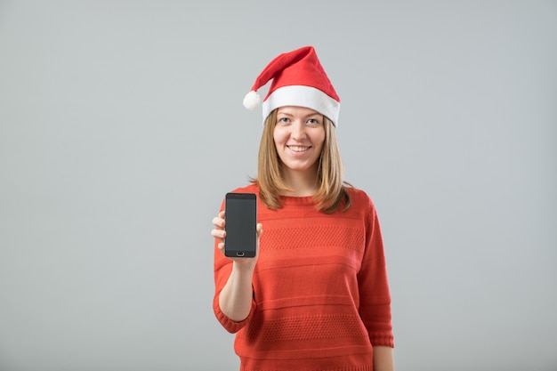 Mujer joven con sombrero de santa mostrando smartphone