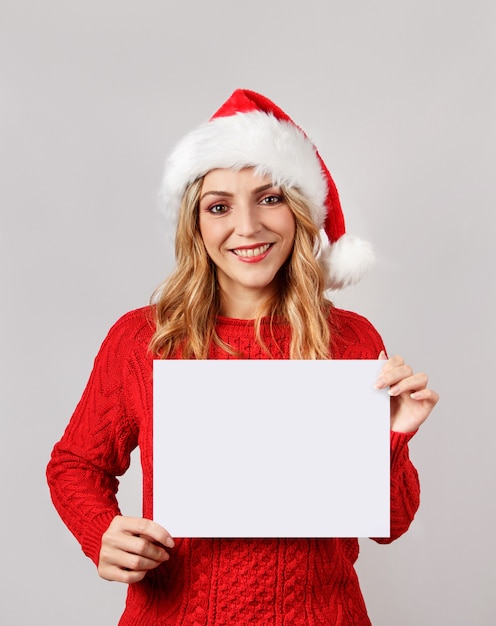 Mujer joven con sombrero de santa sosteniendo papel blanco en blanco