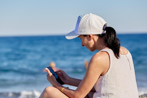 Mujer joven en un sombrero con un teléfono en la playa cerca del mar El concepto de trabajo independiente en línea conferencia en línea o estudiar en línea Foto de alta calidad