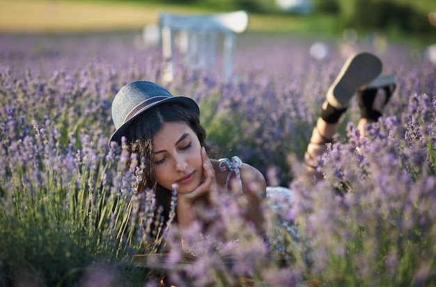 Mujer joven con sombrero tumbado en el campo de lavanda en verano