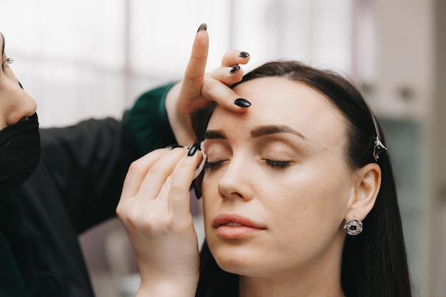 Una mujer joven se somete a un procedimiento de corrección de cejas en un salón de belleza. La niña pinta sus cejas en el salón.