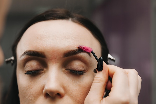 Una mujer joven se somete a un procedimiento de corrección de cejas en un salón de belleza. La niña pinta sus cejas en el salón.