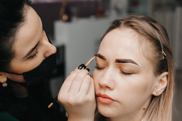 Una mujer joven se somete a un procedimiento de corrección de cejas en un salón de belleza. La niña pinta sus cejas en el salón.