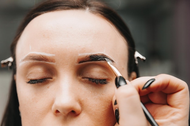 Una mujer joven se somete a un procedimiento de corrección de cejas en un salón de belleza. La niña pinta sus cejas en el salón.