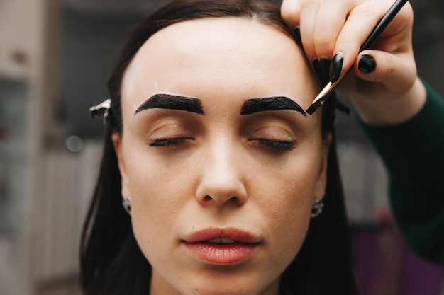 Una mujer joven se somete a un procedimiento de corrección de cejas en un salón de belleza. La niña pinta sus cejas en el salón.