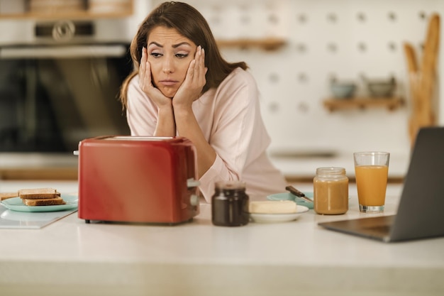 Mujer joven somnolienta preparándose el desayuno mientras se siente cansada, sufre de insomnio y trastornos del sueño.