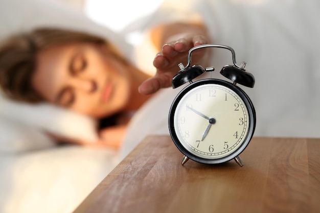 Mujer joven soñolienta estirando la mano para que suene la alarma dispuesta a apagarla Despierta temprano sin dormir lo suficiente conseguir el concepto de trabajo