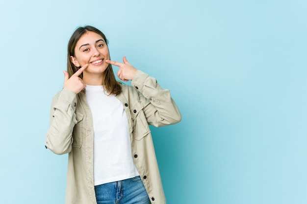 Mujer joven sonríe, señalando con el dedo a la boca