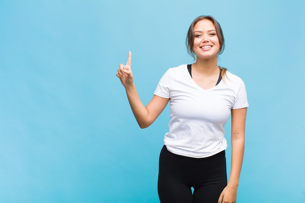 Mujer joven sonriendo alegre y felizmente, apuntando hacia arriba con una mano