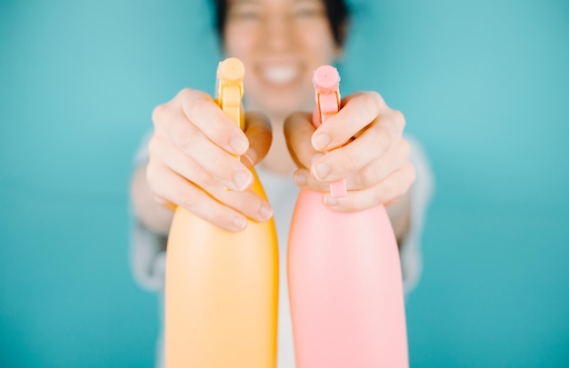Mujer joven sonriendo alegremente a la cámara mientras apunta a la cámara un par de rociadores de agua para refrescarse durante las vacaciones de verano al aire libre con espacio de copiaImagen de fondo de color