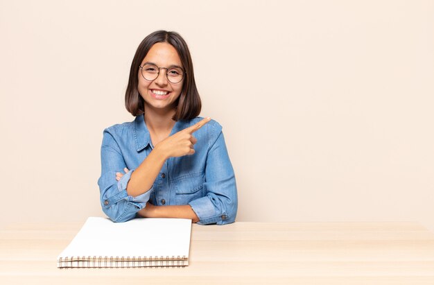 Mujer joven sonriendo alegremente, sintiéndose feliz y apuntando hacia un lado y hacia arriba, mostrando el objeto