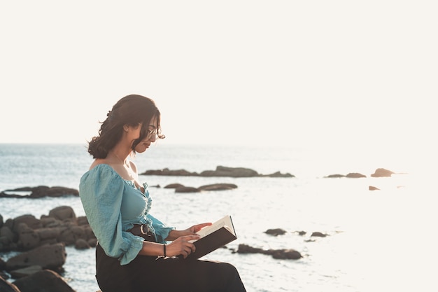 Mujer joven sonriendo a la cámara mientras lee en la playa