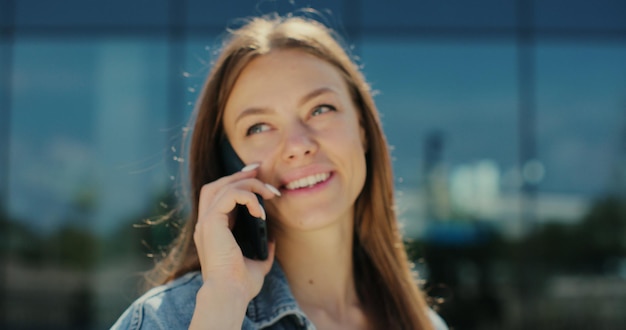 Mujer joven sonriendo confiada hablando en el teléfono inteligente en la calle Retrato cara femenina niña conversando usa el teléfono inteligente en la calle moderna