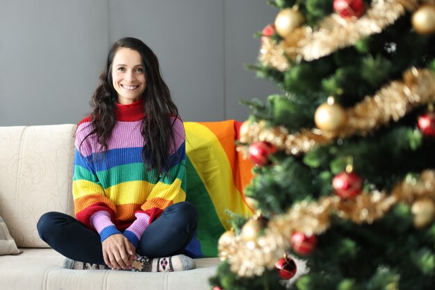 Mujer joven sonriendo y emplazamiento en el sofá cerca del árbol de navidad