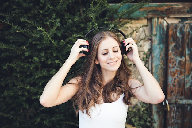 Mujer joven sonriendo y escuchando música a través de auriculares al aire libre