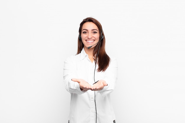 Mujer joven sonriendo felizmente con mirada amable, segura y positiva, ofreciendo y mostrando un objeto o concepto con auriculares y micrófono