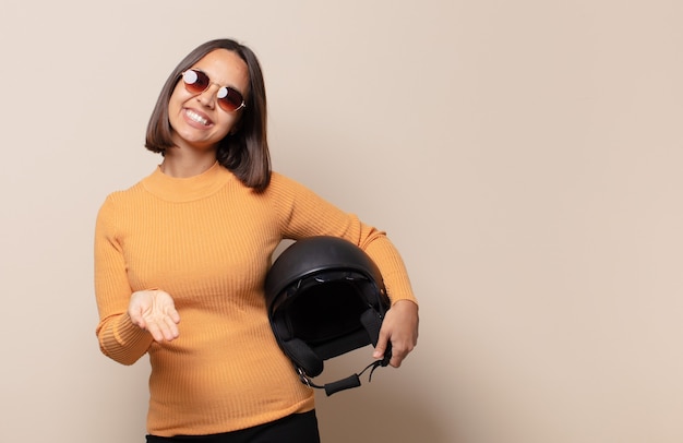 Mujer joven sonriendo felizmente con mirada amistosa, segura y positiva, ofreciendo y mostrando un objeto o concepto