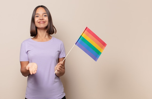 Mujer joven sonriendo felizmente con mirada amistosa, segura y positiva, ofreciendo y mostrando un objeto o concepto