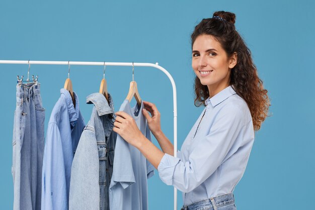 Mujer joven sonriendo mientras elige la chaqueta de jeans en el estante de la tienda