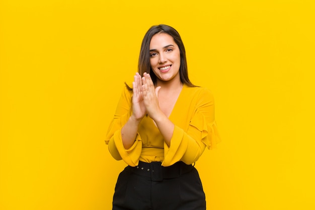 Mujer joven sonriendo y mirando amigable, mostrando el número uno o primero con la mano hacia adelante, cuenta atrás aislado en la pared naranja