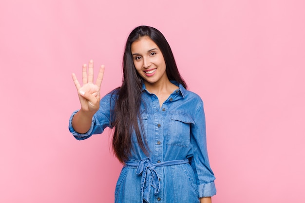 Mujer joven sonriendo y mirando amistosamente, mostrando el número cuatro o cuarto con la mano hacia adelante, contando hacia atrás