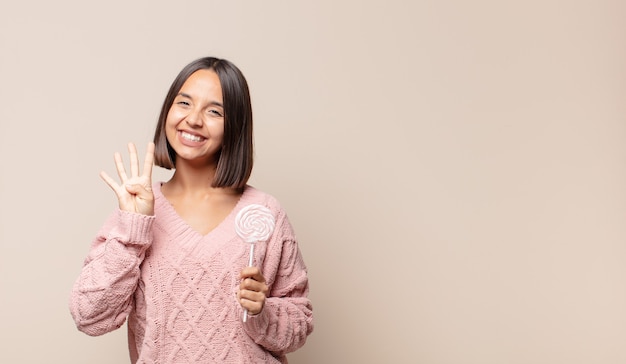 Mujer joven sonriendo y mirando amistosamente, mostrando el número cuatro o cuarto con la mano hacia adelante, contando hacia atrás