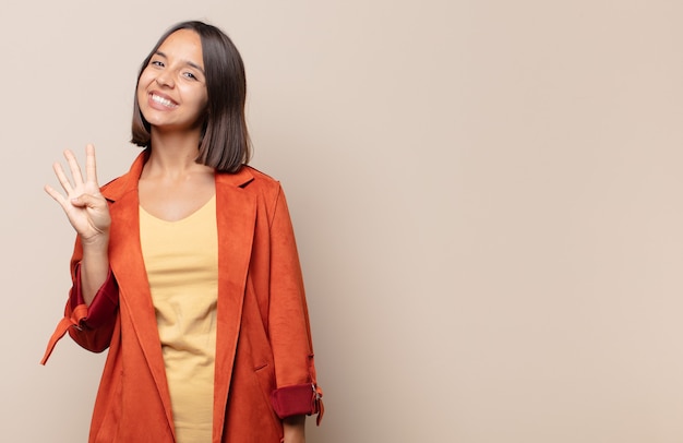 Mujer joven sonriendo y mirando amistosamente, mostrando el número cuatro o cuarto con la mano hacia adelante, contando hacia atrás