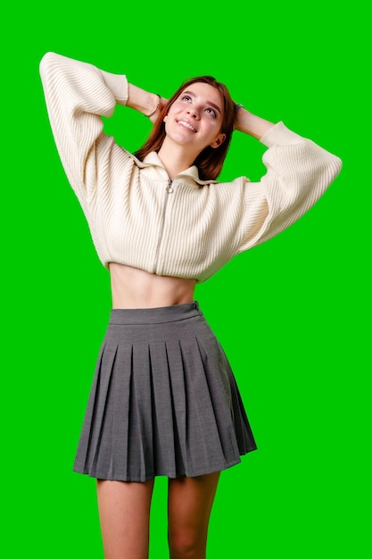 Mujer joven sonriendo y mirando hacia arriba mientras sostiene su cabello sobre un fondo verde