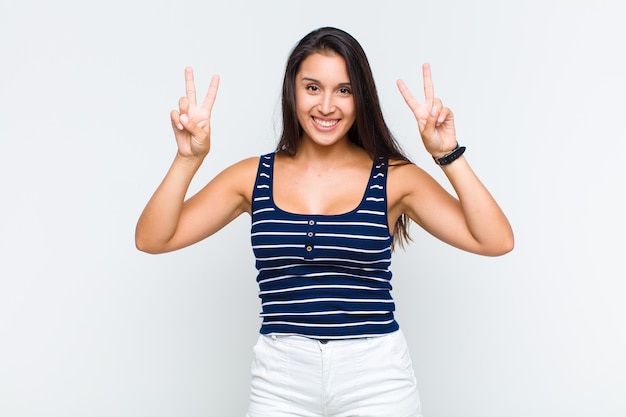 Mujer joven sonriendo y mirando feliz, amigable y satisfecho, gesticulando victoria o paz con ambas manos