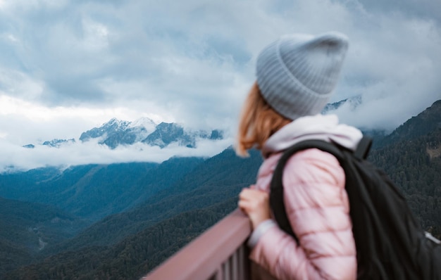 Mujer joven sonriendo con una mochila en un sombrero admirando las montañas Subiendo a la cima un viaje a las montañas un turista en una excursión