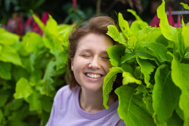 Mujer joven sonriendo en la naturaleza en el parque sobre un fondo de pared verde en su jardín en primavera o