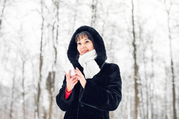 Mujer joven sonriendo con teléfono inteligente y paisaje invernal.