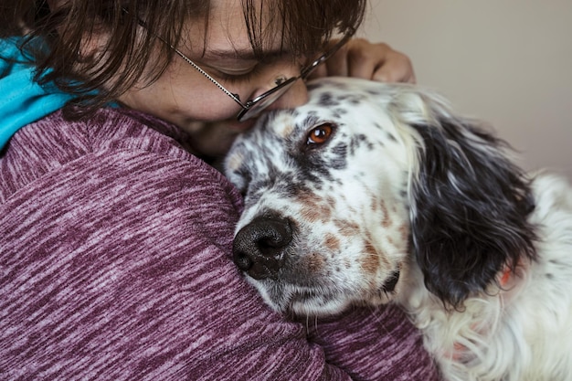 Mujer joven sonriente abrazando al perro setter inglés en primer plano del interior de la casa