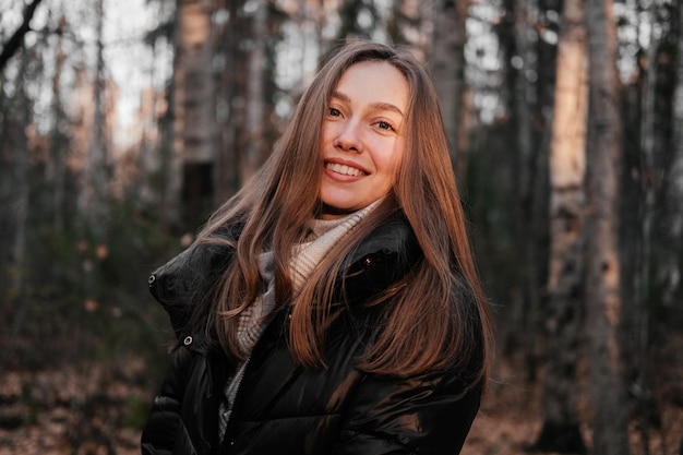 Mujer joven sonriente con abrigo de pie en el bosque de otoño al aire libre