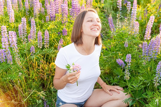 Mujer joven sonriente al aire libre hermosa chica brunete descansando en el campo de verano con flores silvestres en flor...