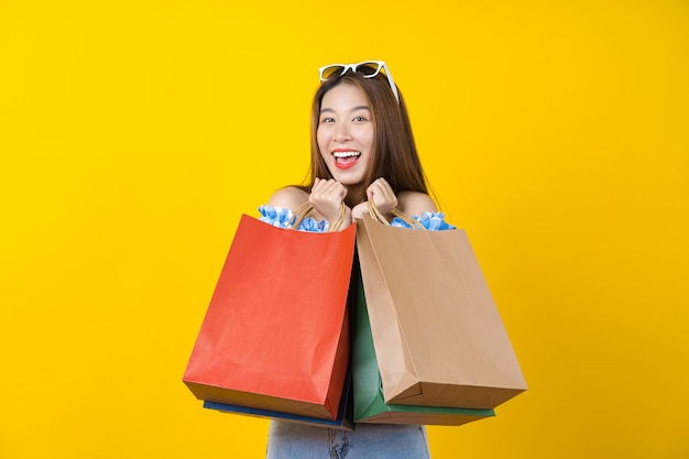 Mujer joven sonriente asiática atractiva que lleva el bolso coloful de compras en color amarillo aisolated