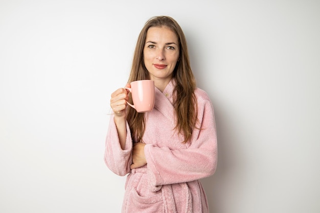 Mujer joven sonriente en una bata de baño con una taza sobre un fondo blanco.