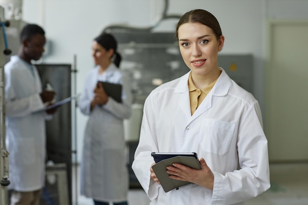 Mujer joven sonriente con bata de laboratorio mirando a la cámara en el taller de la fábrica